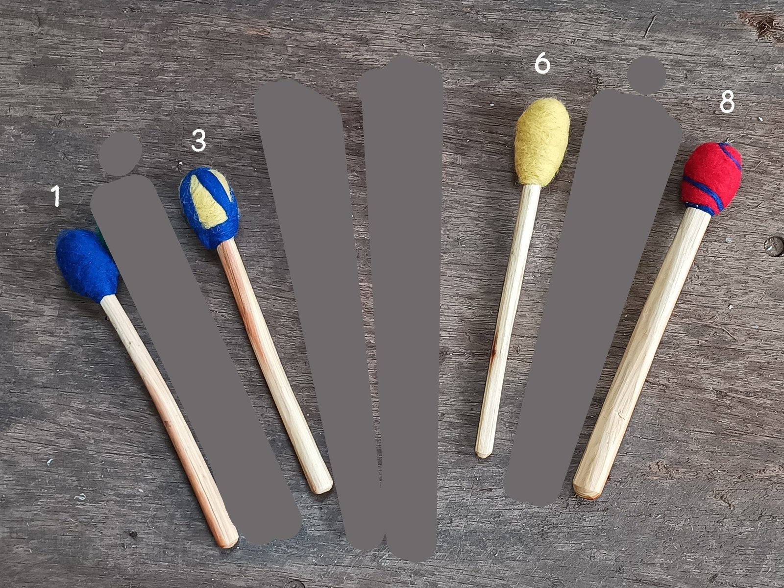 All natural hand drum sticks with colorful felt heads on a wooden surface.