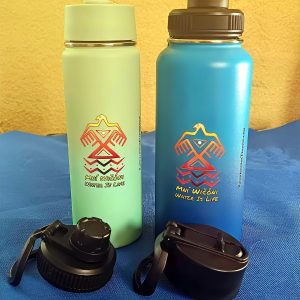 Two Kinnikinnick water bottles with black caps on a blue surface.