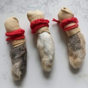Three lucky rabbit foot charms with red yarn and paper bandages on a white surface.